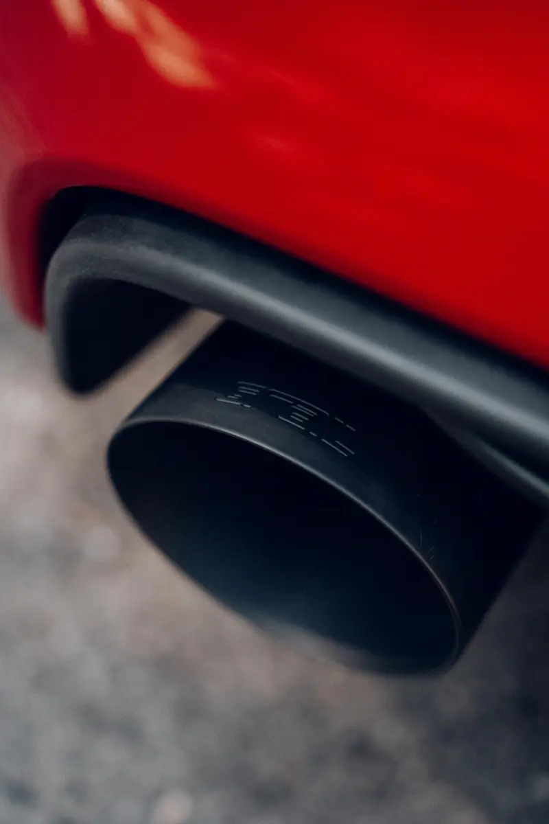 Detail eines schwarzen Auspuffs an einem roten Auto.