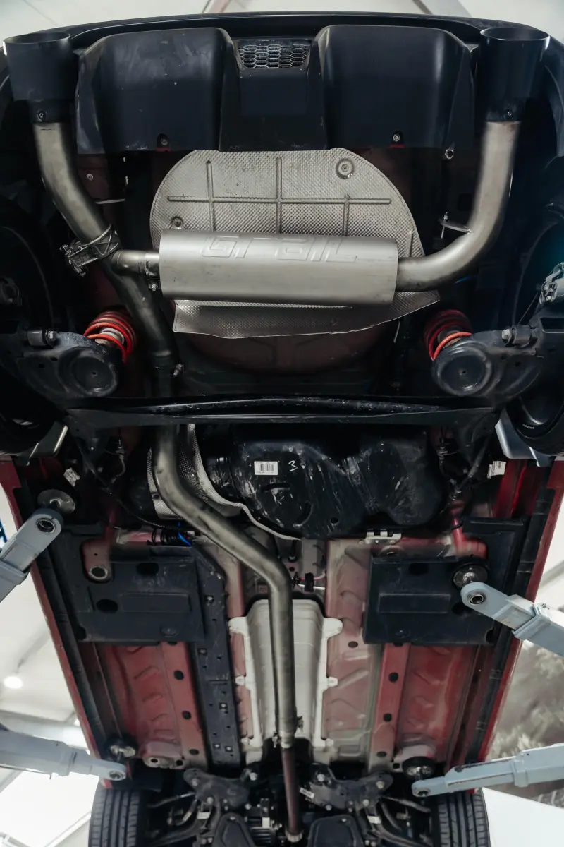 Unterseite eines Autos mit Auspuff- und Fahrwerksteilen.